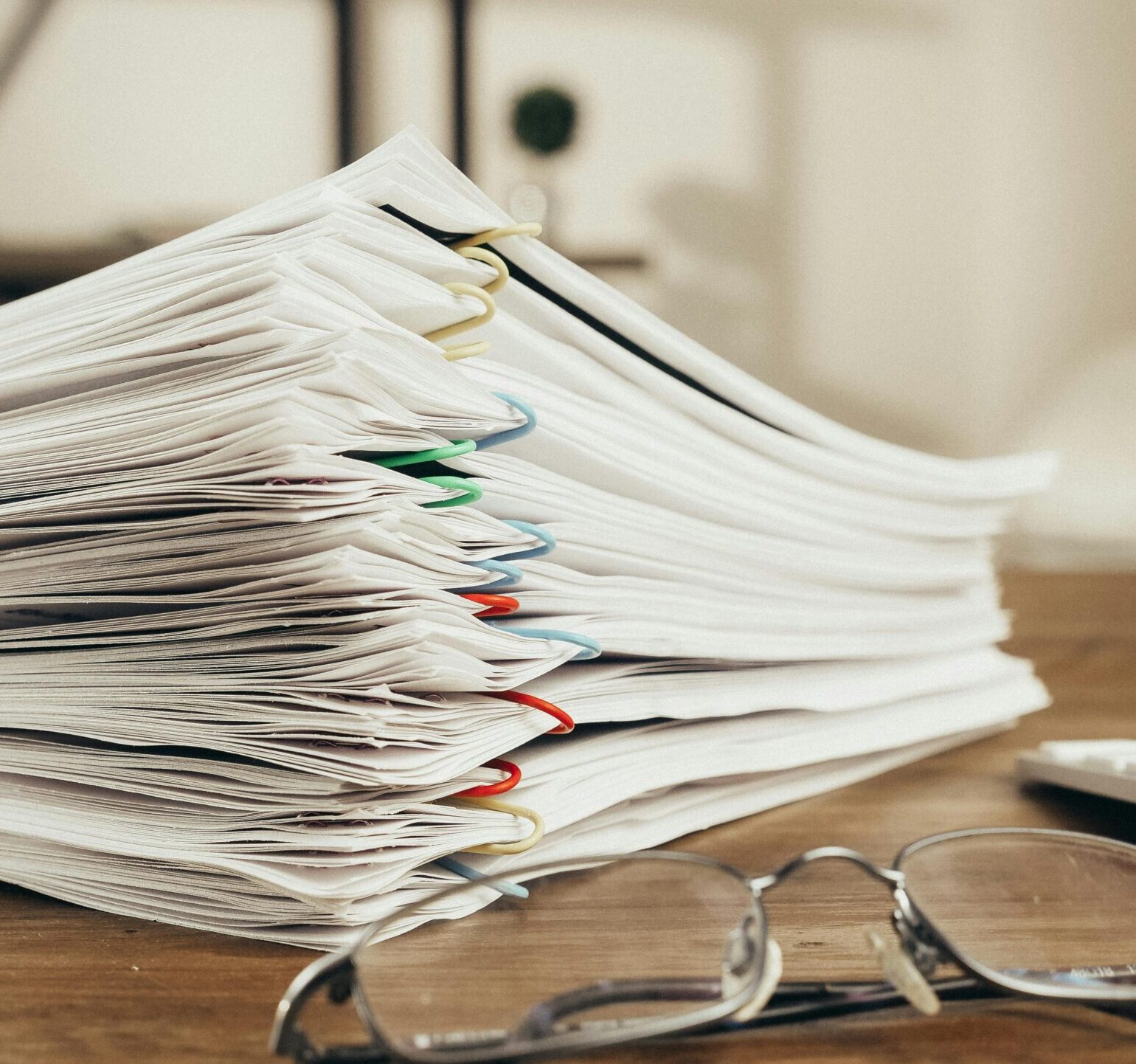 Close-up of a stack of office papers on a desk with glasses, emphasizing organization.